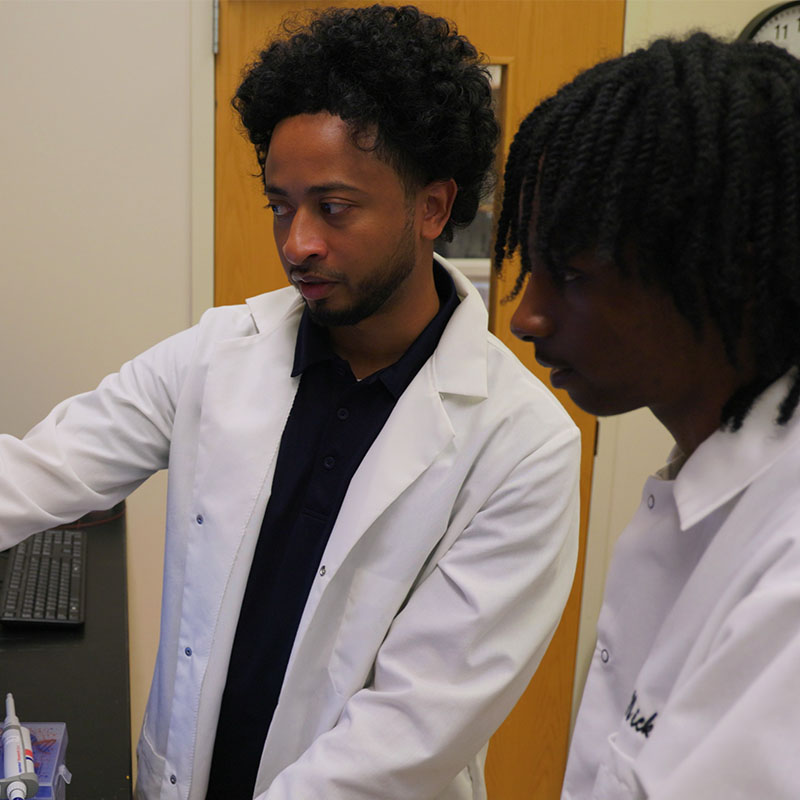 A Project ENGAGES student looks on as his mentor points out something on a machine in a lab. 