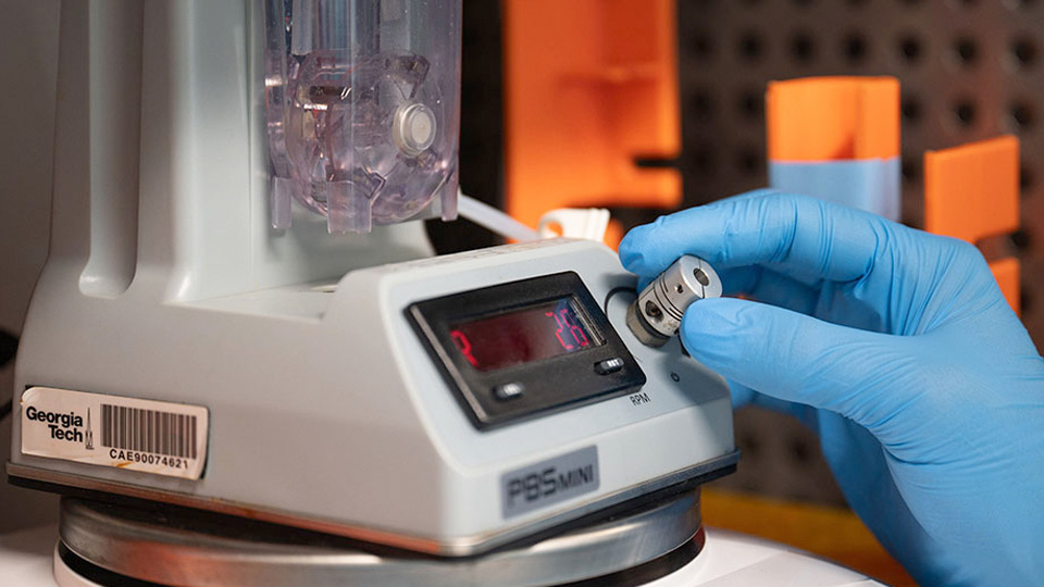 A gloved hand adjusts a control knob on a laboratory mixing or centrifuge device with a digital display, used for precise sample preparation.