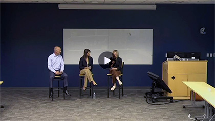 Three speakers seated on stools in a conference room during a panel discussion.